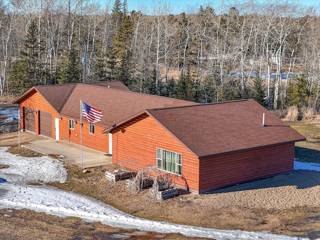 view of side of home featuring a forest view, roof with shingles, an attached garage, and a patio area