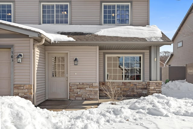 snow covered property entrance with stone siding, a porch, and a garage