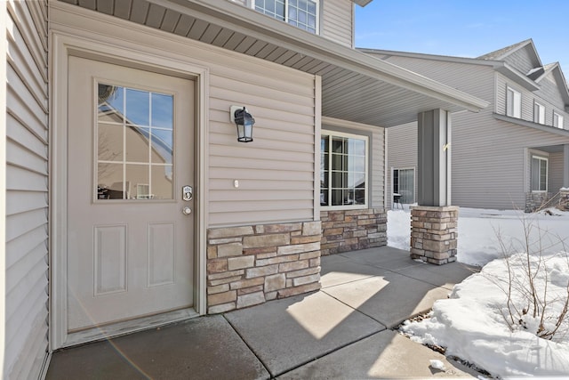 snow covered property entrance featuring covered porch and stone siding