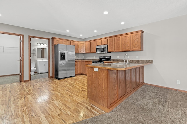 kitchen featuring brown cabinets, a sink, stainless steel appliances, a peninsula, and baseboards