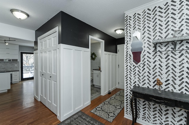 corridor with a wainscoted wall, a textured ceiling, and dark wood-style flooring