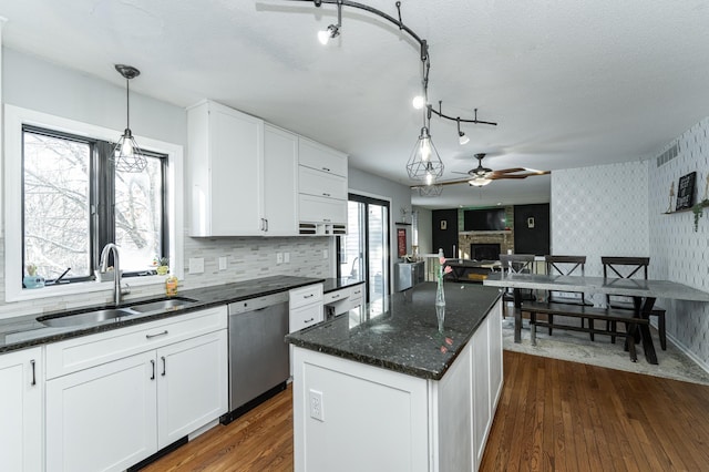 kitchen with wallpapered walls, dark wood finished floors, dishwasher, a stone fireplace, and a sink