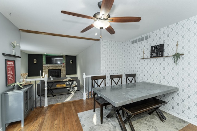 dining area with visible vents, wood finished floors, a fireplace, wallpapered walls, and baseboards