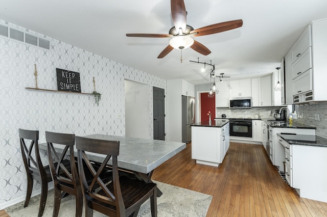 kitchen with a sink, dark countertops, a center island, stainless steel appliances, and wallpapered walls