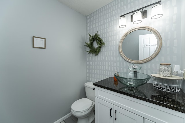 bathroom with wallpapered walls, toilet, vanity, and baseboards