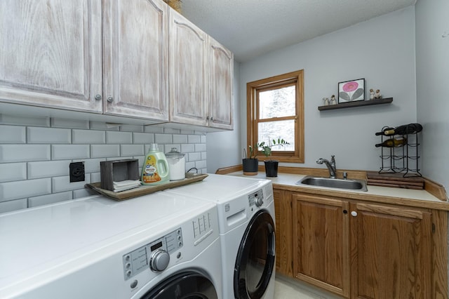 laundry area featuring a sink, cabinet space, a textured ceiling, and washing machine and clothes dryer