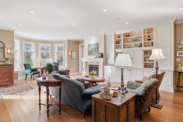 living room featuring light wood-style floors, a glass covered fireplace, and crown molding