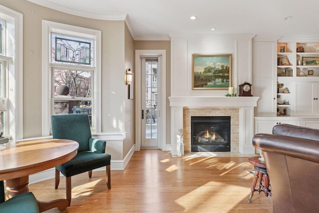 living room with baseboards, recessed lighting, light wood-style floors, a tiled fireplace, and crown molding