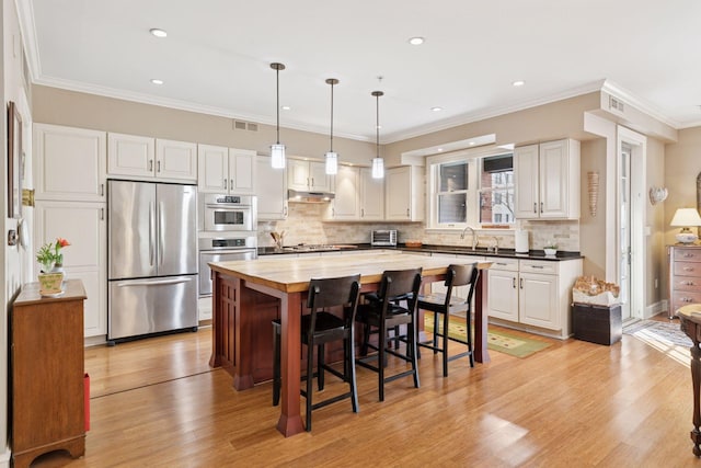 kitchen featuring visible vents, a kitchen bar, stainless steel appliances, wood counters, and a sink