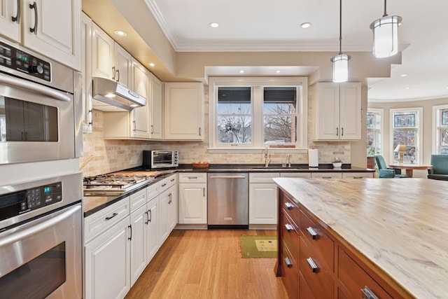 kitchen featuring under cabinet range hood, light wood-style floors, appliances with stainless steel finishes, and crown molding