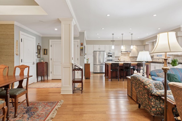 living room with light wood finished floors, recessed lighting, crown molding, and ornate columns