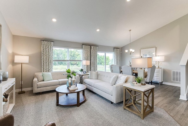 living room featuring lofted ceiling, visible vents, wood finished floors, a chandelier, and baseboards