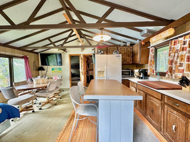 kitchen with vaulted ceiling with beams, open floor plan, a center island, white fridge with ice dispenser, and stainless steel microwave