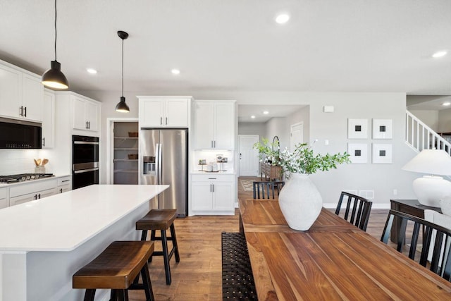 kitchen with stainless steel appliances, a kitchen island, light countertops, light wood finished floors, and a kitchen bar