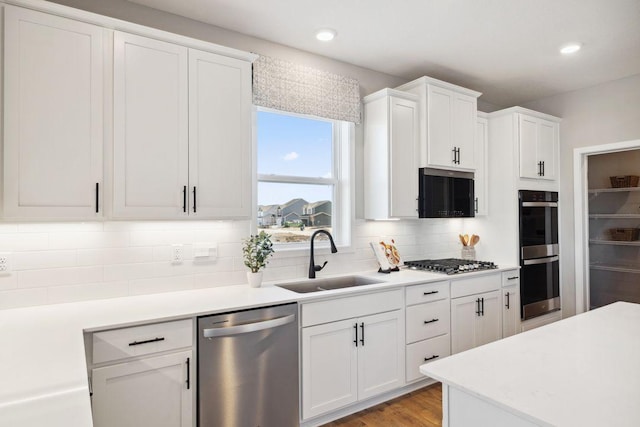 kitchen with stainless steel appliances, white cabinetry, a sink, and backsplash