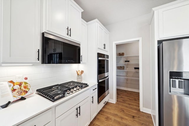 kitchen with stainless steel appliances, light countertops, light wood-style floors, white cabinetry, and backsplash