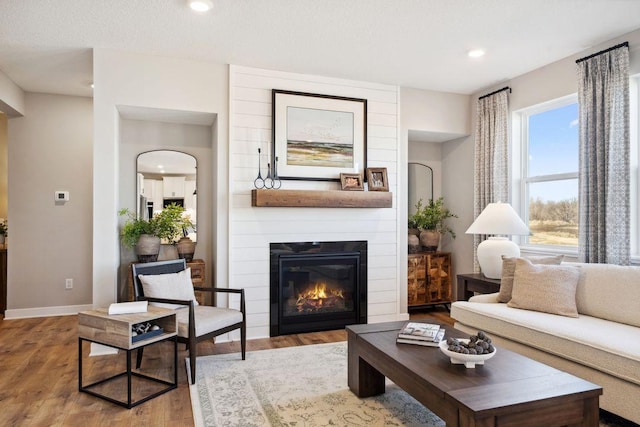 living area with recessed lighting, a large fireplace, baseboards, and wood finished floors