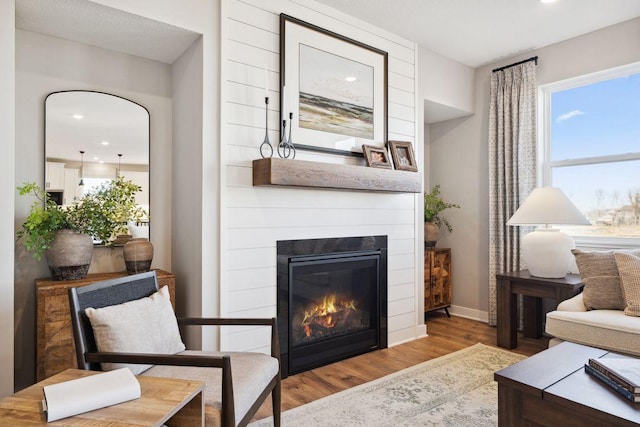 living room featuring wood finished floors, a glass covered fireplace, and baseboards