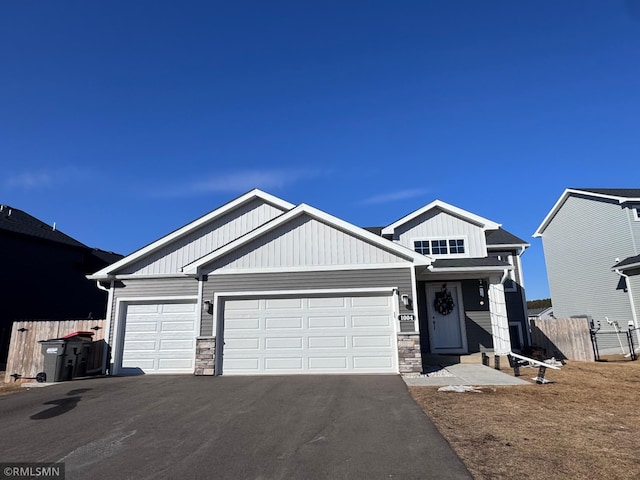 view of front of property featuring aphalt driveway, stone siding, an attached garage, and fence