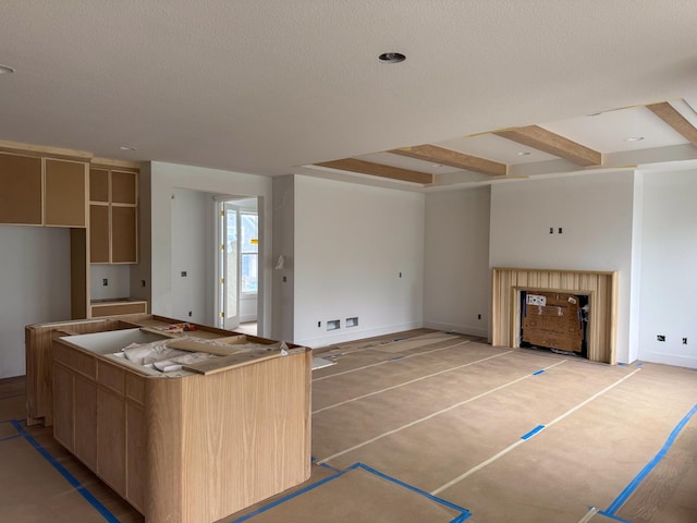 kitchen featuring a textured ceiling, recessed lighting, baseboards, a kitchen island, and beamed ceiling