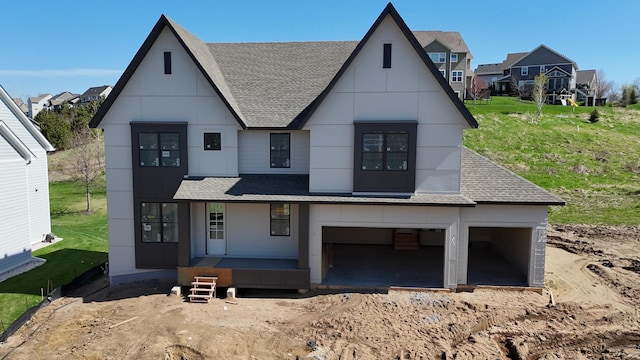 view of front facade with a porch, an attached garage, a front lawn, and roof with shingles