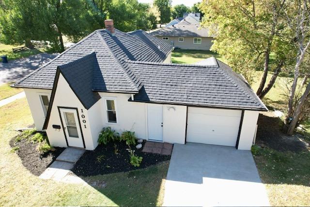 view of front of home with a chimney, an attached garage, concrete driveway, and a shingled roof