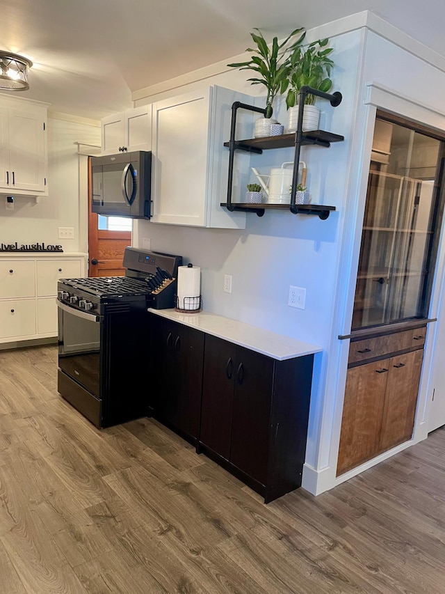 kitchen with light countertops, white cabinets, wood finished floors, black microwave, and gas range