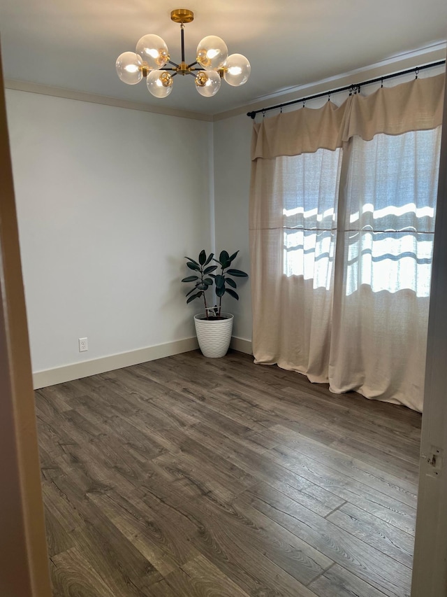 unfurnished room featuring a chandelier, baseboards, dark wood finished floors, and crown molding