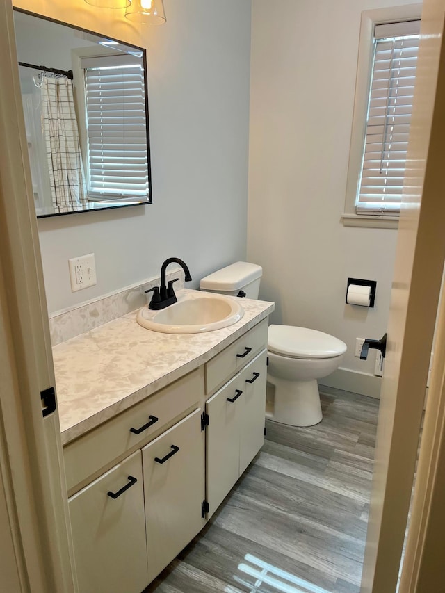 bathroom featuring baseboards, a shower with shower curtain, toilet, wood finished floors, and vanity