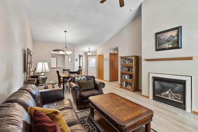 living room featuring ceiling fan with notable chandelier, high vaulted ceiling, light wood-style flooring, and a tile fireplace