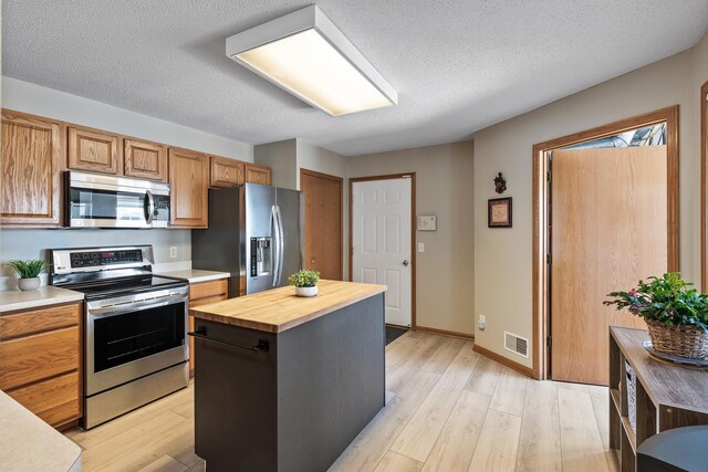 kitchen with visible vents, wood counters, a kitchen island, appliances with stainless steel finishes, and light wood finished floors