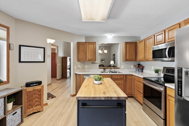 kitchen with light wood finished floors, appliances with stainless steel finishes, a center island, and a sink