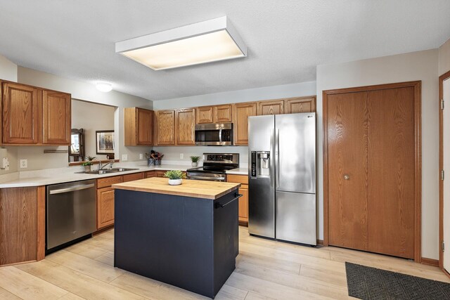 kitchen featuring a kitchen island, light wood-style flooring, a sink, appliances with stainless steel finishes, and wood counters