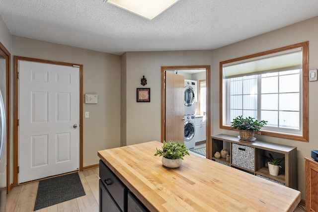 entryway with stacked washer / dryer, light wood finished floors, and a textured ceiling