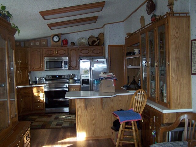 kitchen with wallpapered walls, dark wood-style floors, stainless steel appliances, a peninsula, and light countertops