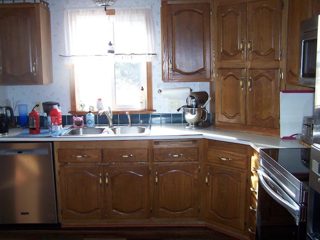 kitchen featuring wallpapered walls, light countertops, brown cabinetry, stainless steel appliances, and a sink