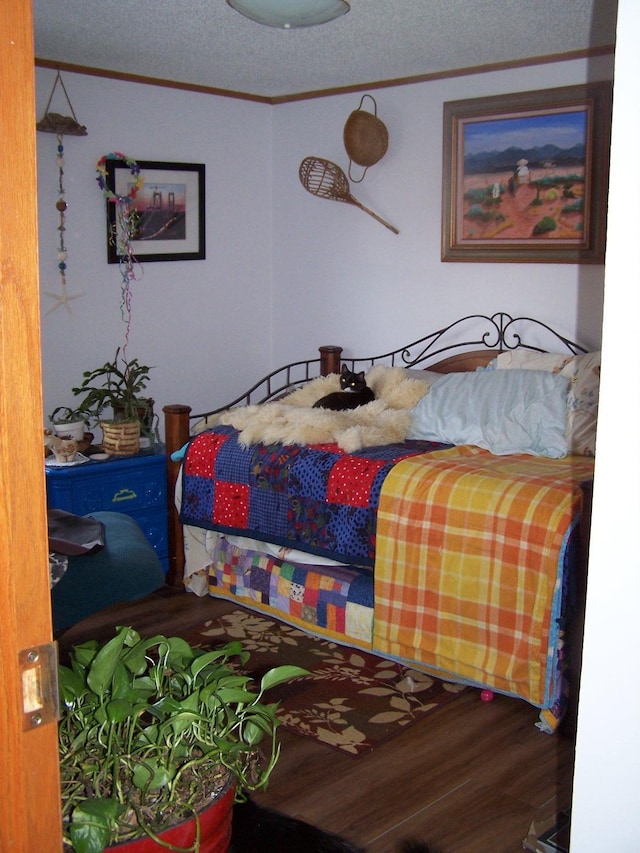 bedroom featuring a textured ceiling, wood finished floors, and ornamental molding