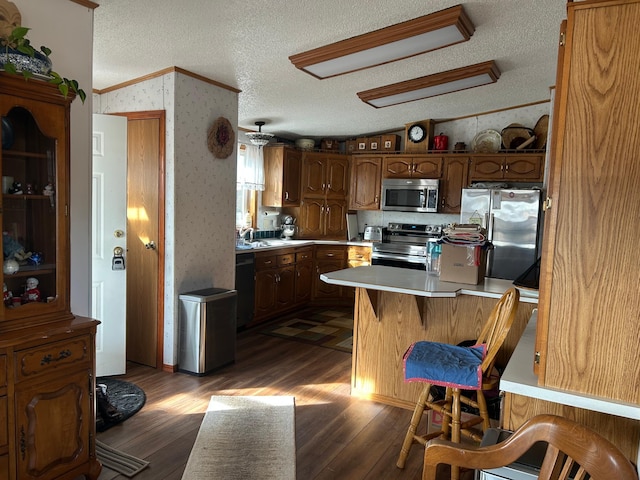 kitchen featuring dark wood-type flooring, wallpapered walls, a textured ceiling, stainless steel appliances, and light countertops