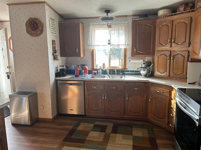 kitchen with a sink, wallpapered walls, a textured ceiling, appliances with stainless steel finishes, and light countertops