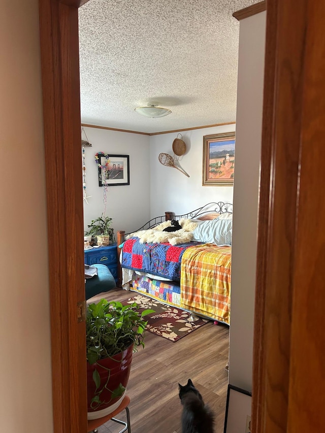 bedroom featuring ornamental molding, a textured ceiling, and wood finished floors