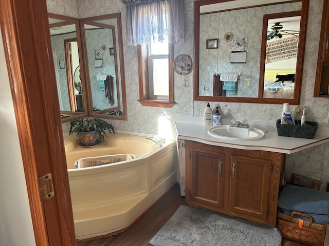 full bathroom featuring a garden tub, a ceiling fan, wood finished floors, wallpapered walls, and vanity