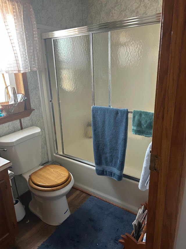 full bath with bath / shower combo with glass door, wood finished floors, vanity, and toilet