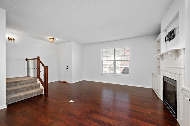 living area featuring a glass covered fireplace, stairway, baseboards, and dark wood-style flooring