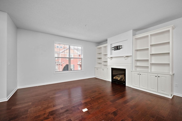 unfurnished living room featuring dark wood-style floors, a tile fireplace, a textured ceiling, and baseboards