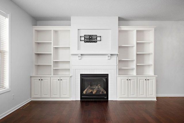 unfurnished living room with visible vents, a textured ceiling, dark wood-style floors, a glass covered fireplace, and baseboards