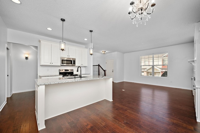 kitchen with a sink, light stone countertops, hanging light fixtures, stainless steel appliances, and dark wood-style flooring