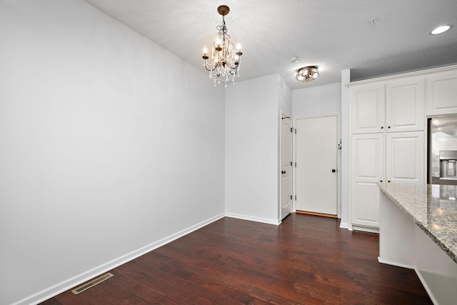 unfurnished dining area with an inviting chandelier, dark wood-type flooring, baseboards, and visible vents