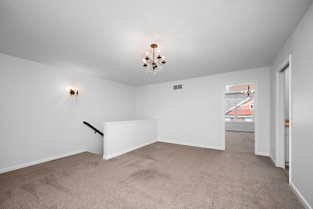 empty room with visible vents, a notable chandelier, a textured ceiling, carpet, and baseboards