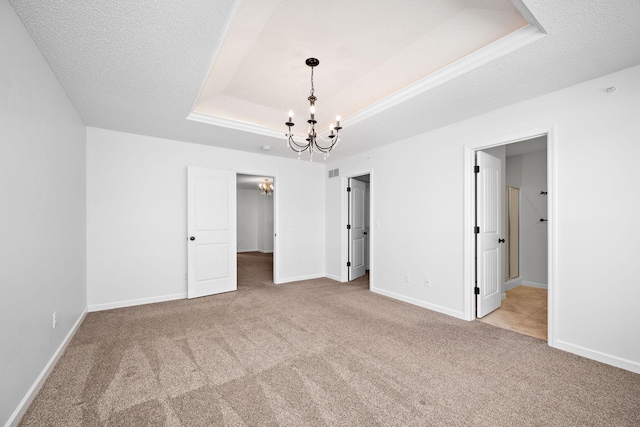 unfurnished bedroom with carpet, baseboards, a tray ceiling, a textured ceiling, and a chandelier