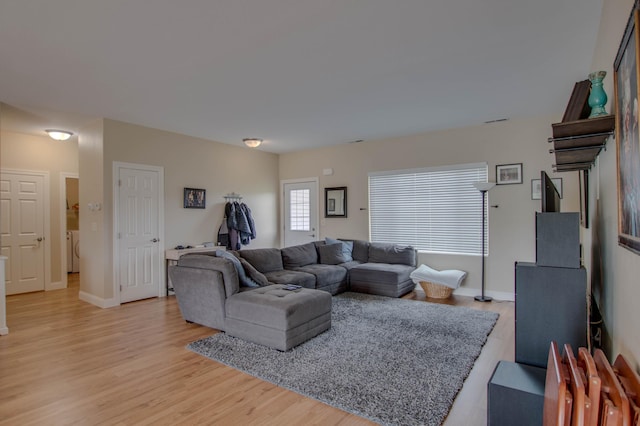 living room featuring light wood-type flooring, visible vents, baseboards, and washer and clothes dryer